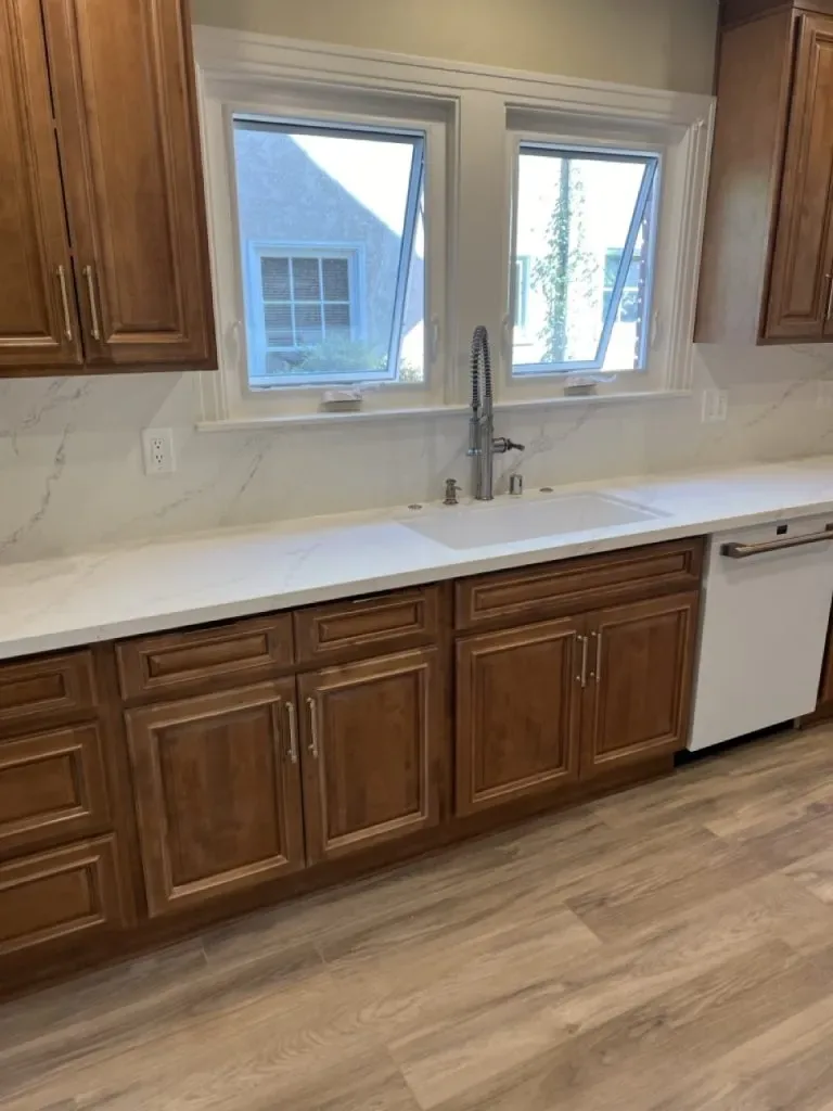 Kitchen sink under a double window with stone counters and wood cabinets