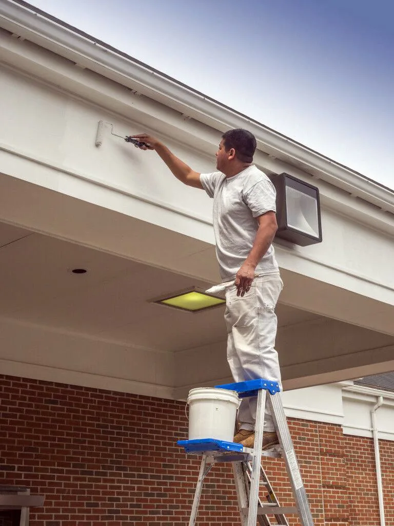 Painter on a ladder rolling paint under a roofline